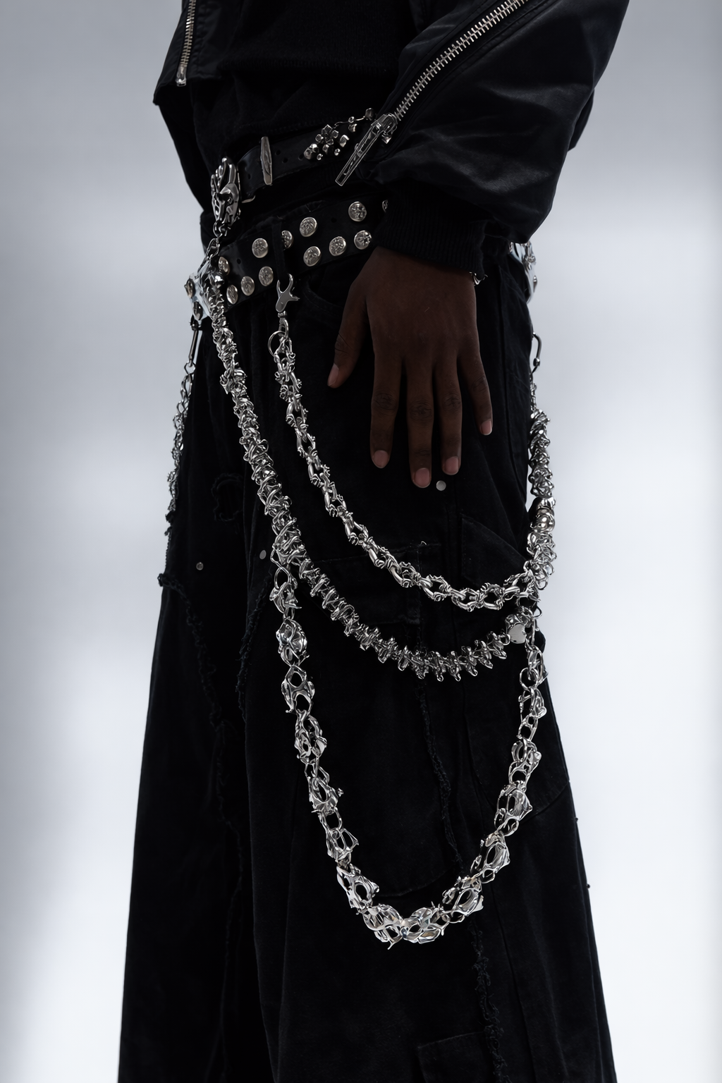 Person wearing a black coat with silver chains and buttons on a white background