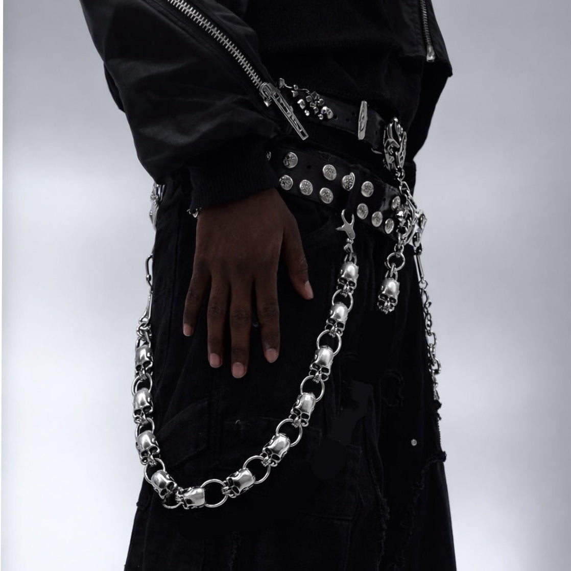 Person wearing a black outfit with silver chain and skull belt detail on a gray background